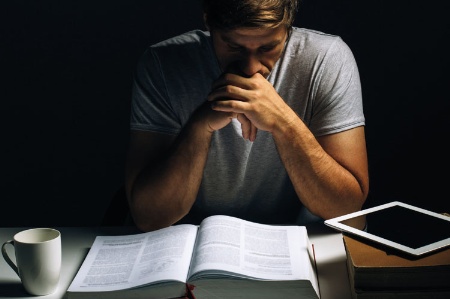 Young man reading book at desk in darkened room