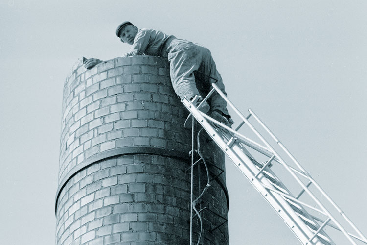 A man standing on a ladder at the top of a chimney