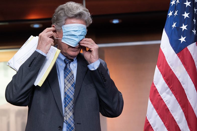 man puts on mask beside US flag