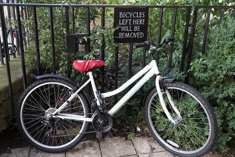 Bicycle parked and locked underneath a Bicycles left here will be removed sign.