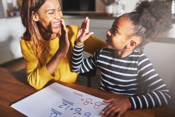 A woman high fives her daughter while she does her homework