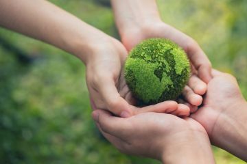 Two pairs of hands hold a tennis ball-sized green globe of the world