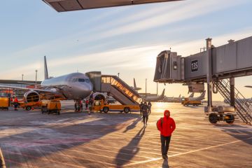 Front view big modern passenger aircraft approach boarding with stairs vehicle against airport building morning evening warm sun.