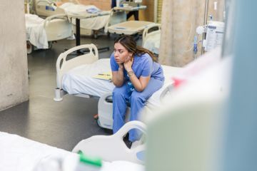 A doctor sits on an empty bed looking worried