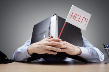 A man covers his head with his laptop and holds a flag that says 'Help!'