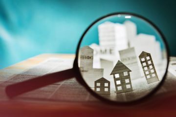 A view through a magnifying glass shows houses made of paper