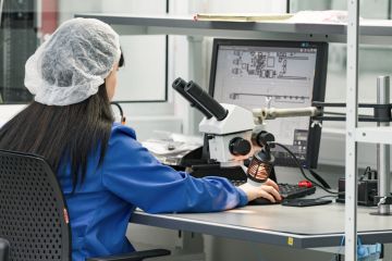 Control operator checks finished circuit board in plant for production of electronic equipment.