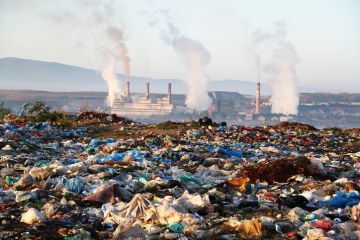 Factory chimneys behind a rubbish dump, illustrating exploitative capitalism