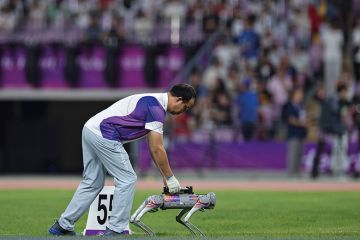 A referee puts a discus onto a robot dog at an athletics meeting