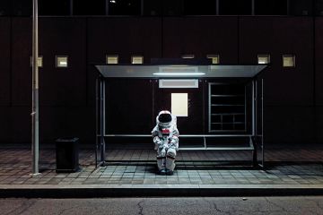 An astronaut sits at a bus stop to illustrate being left behind