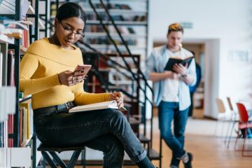 A female student on her phone while a male student reads a book