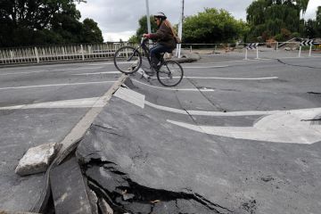 Tania Flowers rides her bike onto a damaged bridge over the Avon River to illustrate New Zealand scraps research reforms and infrastructure funding