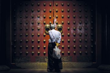 A person looks though the gap in the Buddhist temples giant red doors to illustrate Scholar ‘disinvited’ from conference ‘over husband’s activism’