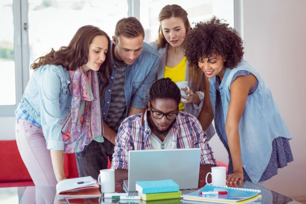 A group of students gathered around a laptop