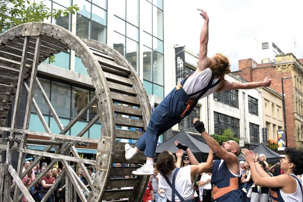  A performer on a rolling wooden wheel falls backwards, knowing that her team members will catch her