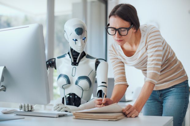 AI robot sat at a computer, while a woman in glasses sits next to pointing at a paper