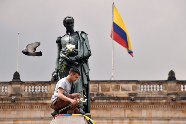 A colombian youngster places the national flag and a bunch of white flowers at the bottom of Simon Bolivar's monument in Bogota.