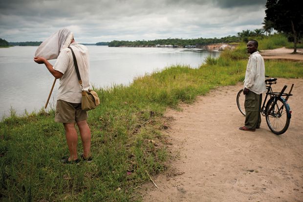 A man looks on in amusement as Ashley Kirk-Spring, a British scientist studying flies beside the Lomami River in DRC, has to put his head right into the net he has caught them in to examine them closely