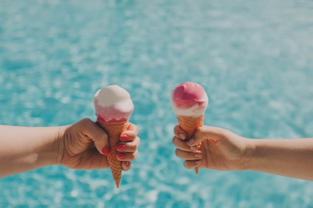 Two hands hold two ice creams by a pool