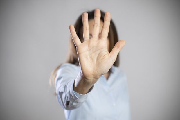 A woman holds her hand out in front of her face to say 'stop'