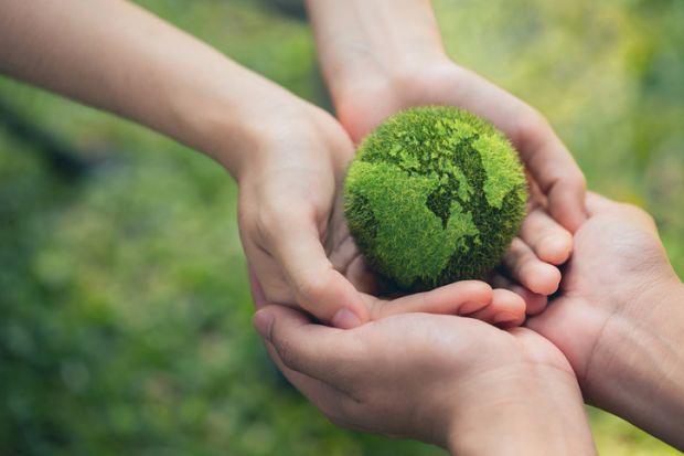 Two pairs of hands hold a tennis ball-sized green globe of the world