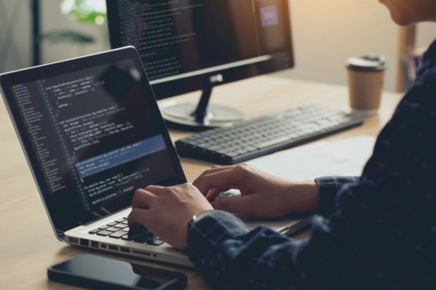 Man sits at desk, typing into a laptop