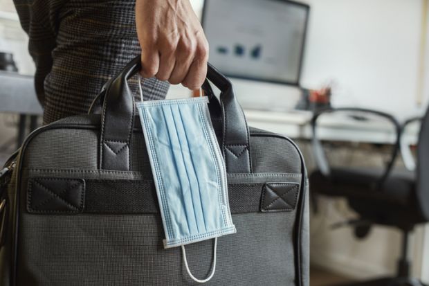 A person carrying a surgical mask and a briefcase, symbolising working during the Covid-19 pandemic