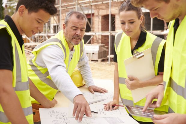 Young builders study blueprint on a building site, illustrating workplace learning