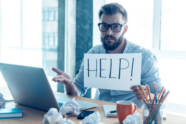 Man at desk holding 'Help' sign