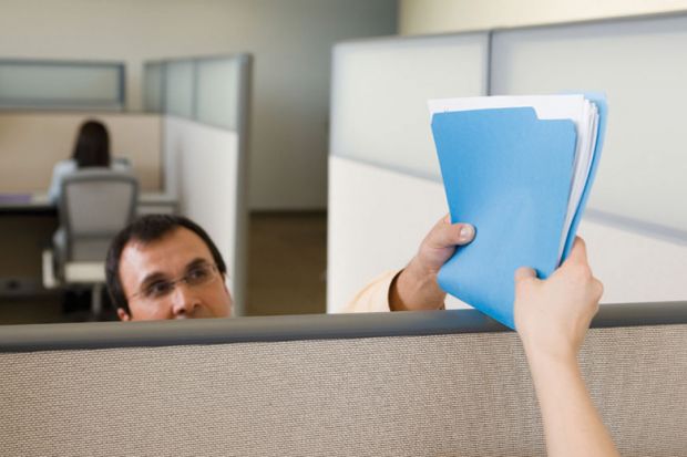 Man handing file/documents to colleague over office partition