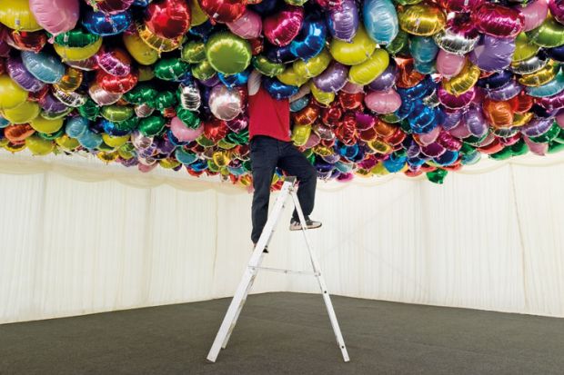 Man on ladder with head in balloons