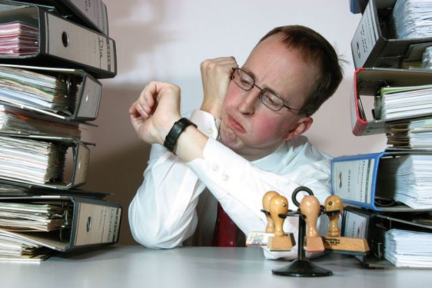 Man sat between piles of files looking at watch