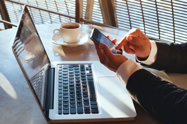 Man using Apple iPhone smartphone and MacBook laptop