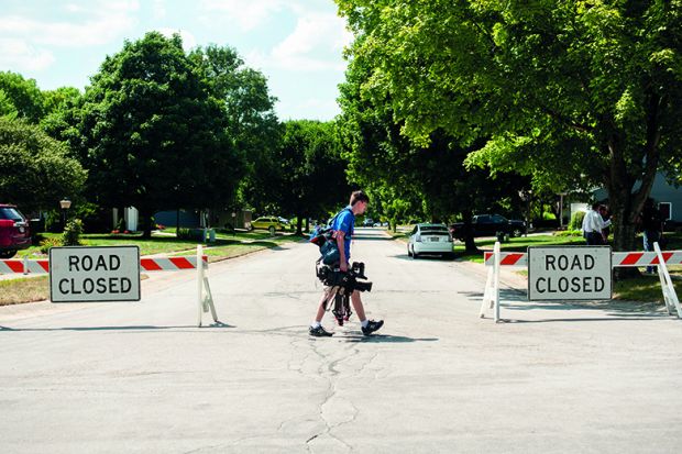 News cameraman walking across empty road with "road closed" sign. To illusatrte covering a "news desert"