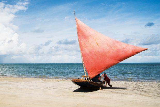 People pushing sailboat from sea onto beach