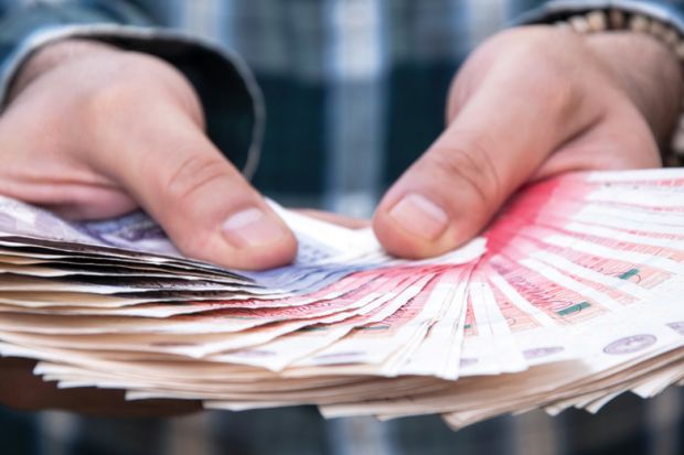 Person holding large fan of British currency in hands