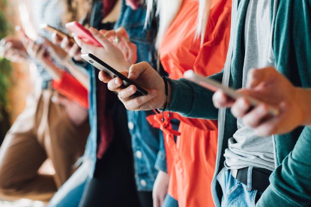 A row of young people on their phones, signifying social media addiction