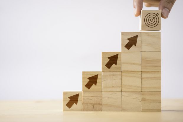 Wooden bricks with arrows pointing upwards towards a target, symbolising promotion