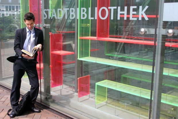 A suited man reads a book outside an empty bookshop