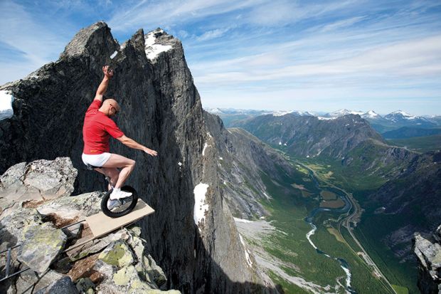 Man riding unicycle at edge of mountain