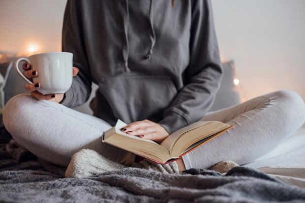 Woman reading book and drinking tea on bed