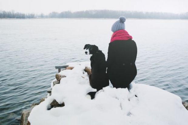 Woman and dog sitting on a snowy river bank 