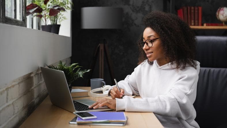 Smiling girl working on laptop and taking notes